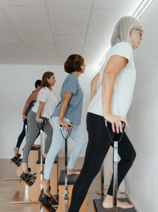 Grupo de alumnas practicando ejercicios de piernas en sillas de Pilates (Wunda Chair) junto a la pared