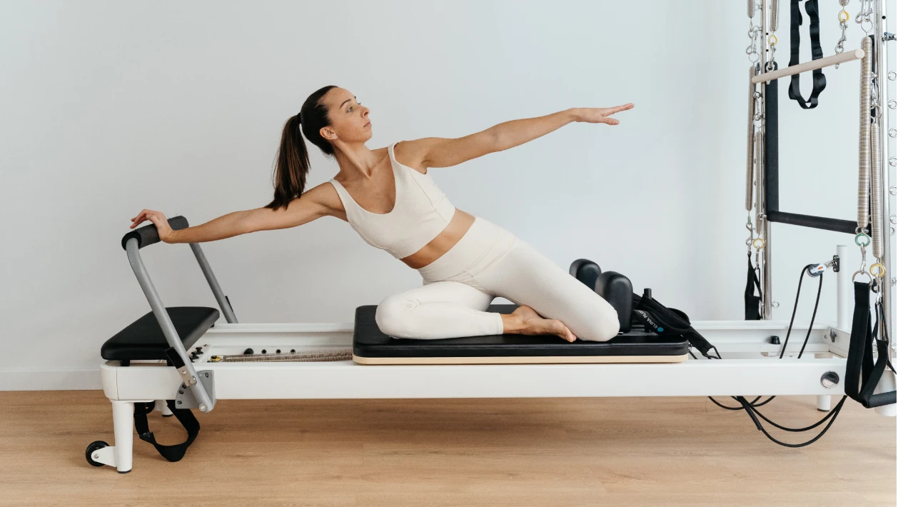 Instructora demostrando estiramiento lateral mermaid sobre el reformer