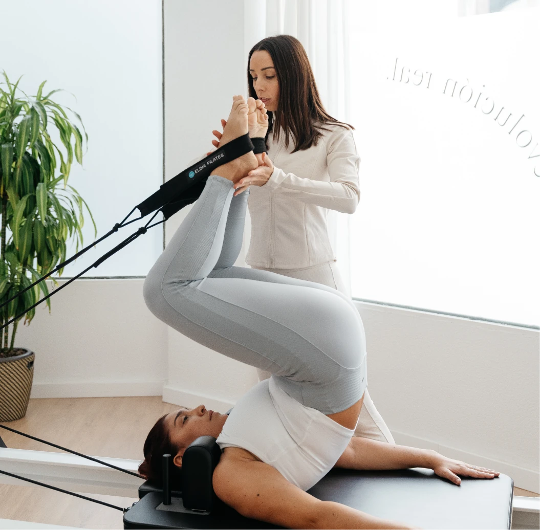 Instructora de ELIX Pilates asistiendo a una alumna en ejercicio de elevación de piernas con correas
